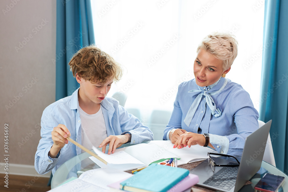 Obraz premium young teacher woman help teen boy to do homework, caucasian pupil and tutor sit at table at home, education concept