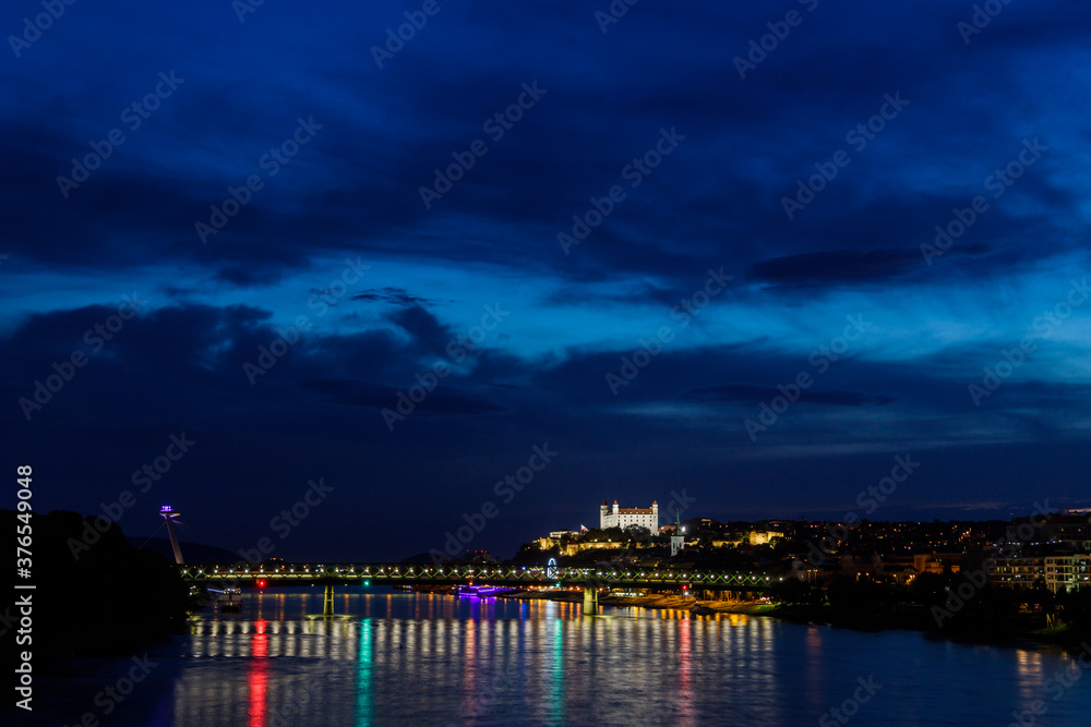 Night over Danube river with lightened castle and SNP bridge, known landmarks in Bratislava, capital of Slovakia. Reflection of lights in water surface.