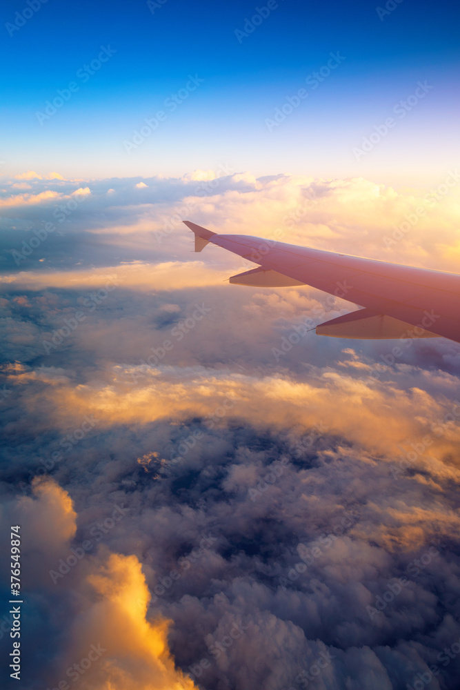 Obraz premium Flying and traveling, view from airplane window on the wing on sunset time. Aircraft wing under the earth and clouds. Flight in sky. Looking over aircraft wing in flight.