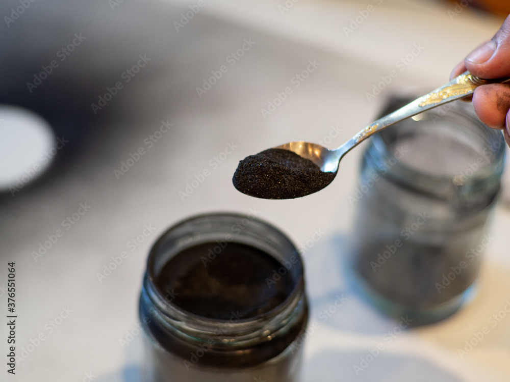 Homemade face masks and scrub with activated powder in glass jar on white background, iron spoon with charcoal Homemade face masks and scrub with activated powder in glass jar on white background, iron spoon with charcoal