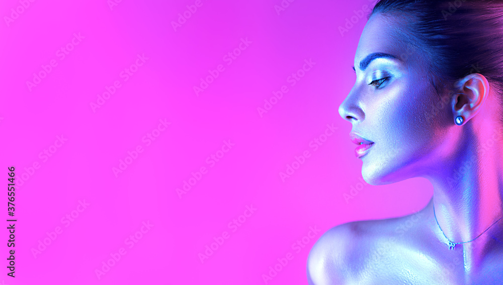 Colorful portrait of a beautiful young woman over purple background. High Fashion model girl in colorful bright neon lights posing in studio, night club. Portrait of beautiful girl in UV. Art design - obrazy, fototapety, plakaty 