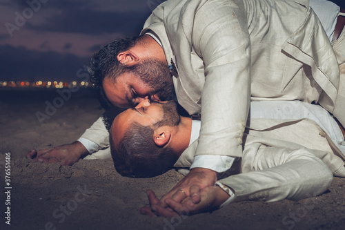 Gay couple kiss on the beach lying on the sand at night