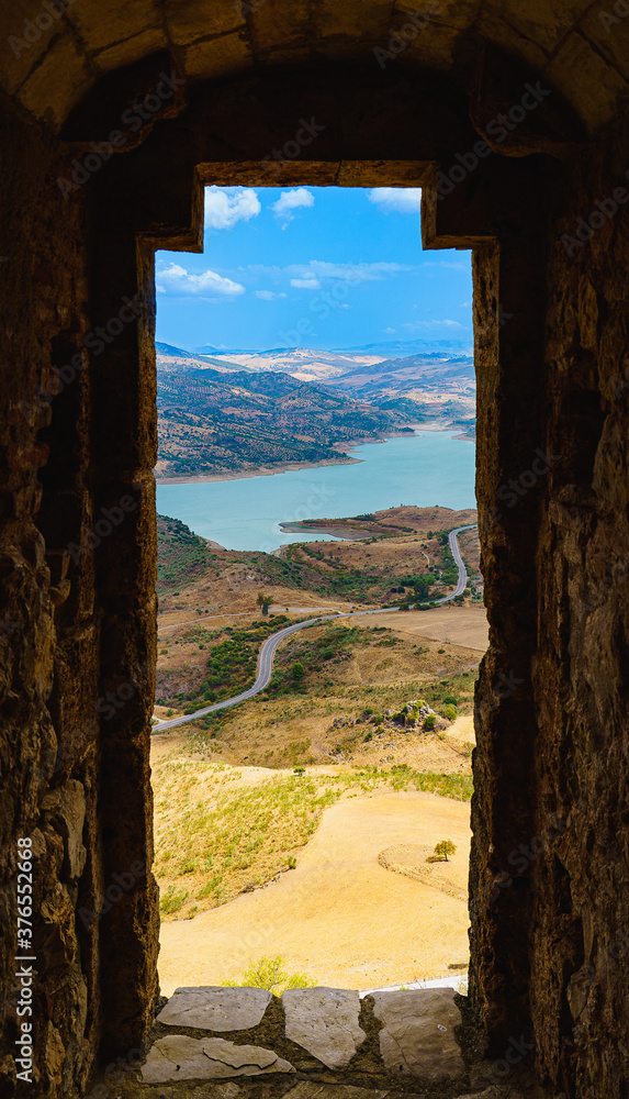 vertical window framed view of turquoise lake, fields, road and mountains in the background