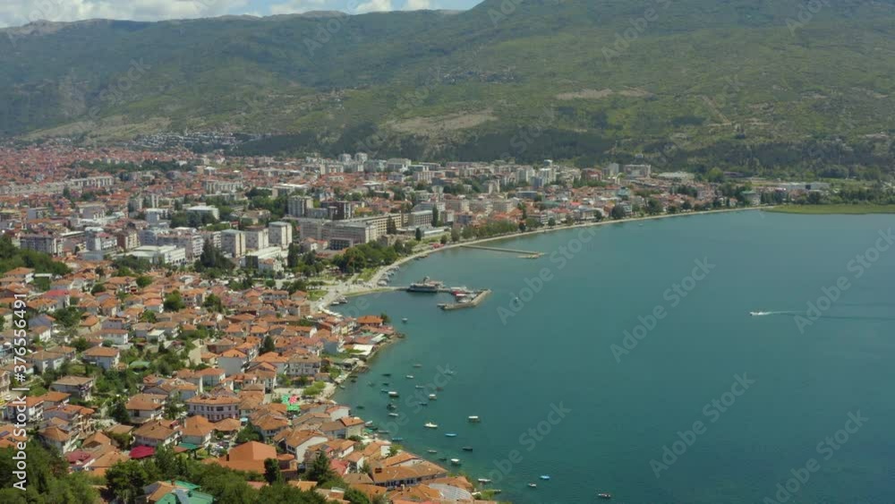 Drone video of an ancient city with houses with red roofs standing on the shores of Lake Ohrid with a shoreline and piers with boats, surrounded by mountains. Aerial view of Ohrid Macedonia.
Drone video of an ancient city with houses with red roofs standing on the shores of Lake Ohrid with a shoreline and piers with boats, surrounded by mountains. Aerial view of Ohrid Macedonia.