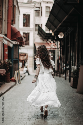 Young beautiful hippy girl runing back and wearing boho style white clothes and accessories. Free spirit concept.