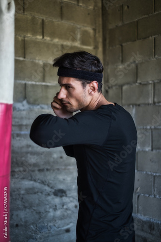 A handsome man in a black shirt punching a boxing bag