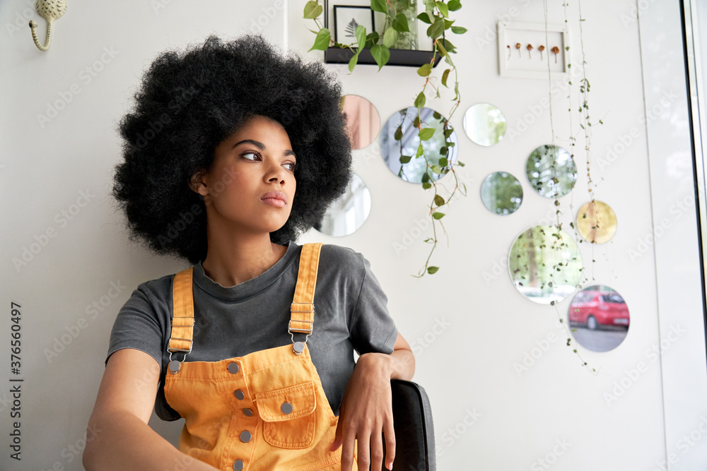 Young thoughtful pensive stylish African American gen z female hipster woman with afro hair looking through window thinking reflecting sitting lost in thoughts at home, in modern cafe alone indoors. - obrazy, fototapety, plakaty 