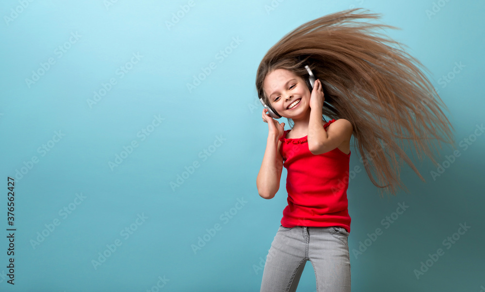 Little cheerful girl with long hair in gray headphones listens to music, dances and has fun. Little cheerful girl with long hair in gray headphones listens to music, dances and has fun.
