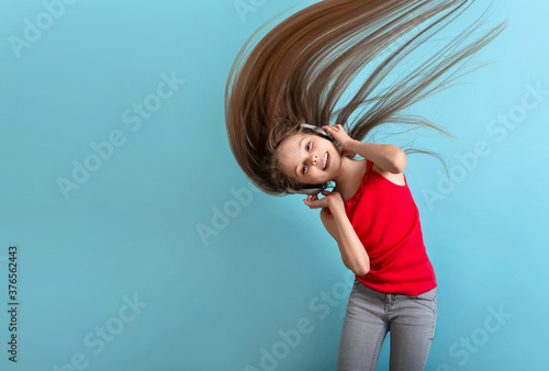 Little cheerful girl with long hair in gray headphones listens to music, dances and has fun.