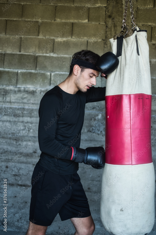 A handsome man in a black shirt punching a boxing bag