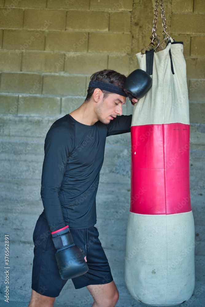 A handsome man in a black shirt punching a boxing bag