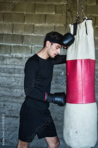 A handsome man in a black shirt punching a boxing bag © Alipasha
