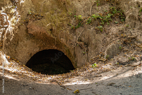 Leon, Nicaragua - November 27, 2008: Ruins of old Leon. Entrance hole to man-made cavern under brown dirt with some green foliage. photo