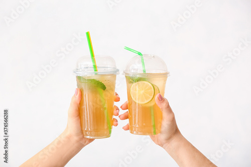 Female hands with cups of tasty cold ice tea on white background