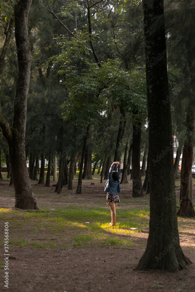 Mujer morena joven disfrutando del aire libre en un parque con muchos arboles.
