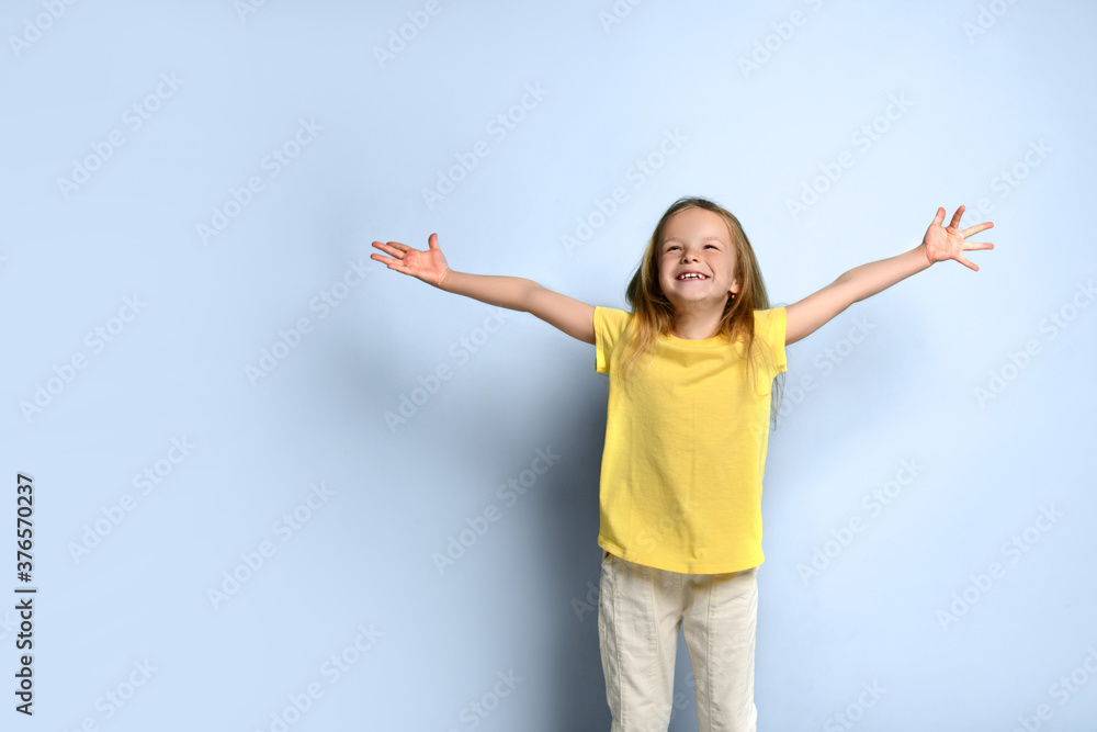 Little female in yellow t-shirt and white pants. She spreading her hands wide apart and screaming, posing on turquoise background. Close up Little female in yellow t-shirt and white pants. She spreading her hands wide apart and screaming, posing on turquoise background. Close up