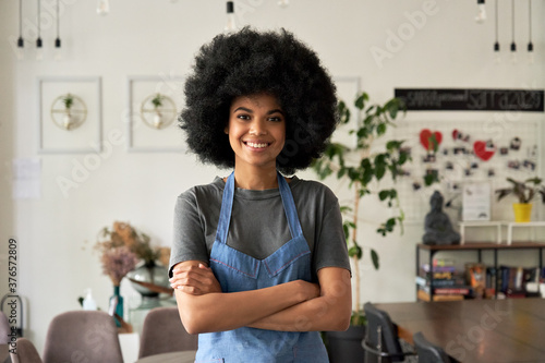 Happy African American young woman with Afro hair modern cafe small business owner, female waitress in reopened restaurant looking at camera standing arms crossed in cozy cafe interior. Portrait. photo