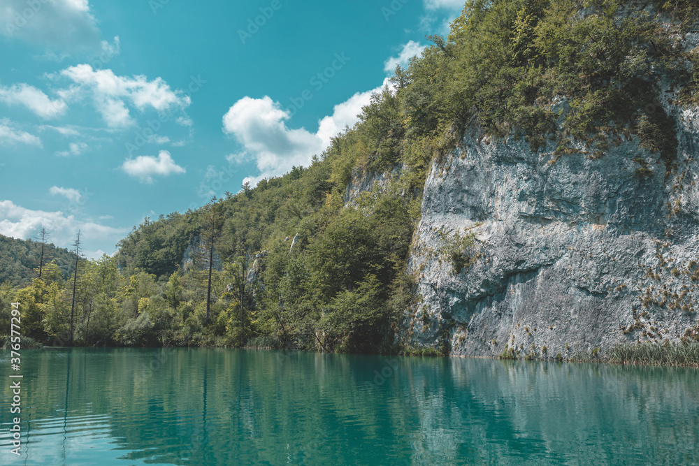 Plitvice Lakes breathtaking waterfalls view. Wild blue green heart of mountains sheltered by rocky walls of mountains. Mountain waters gathered in white foamy waterfalls overflows in beautiful lake