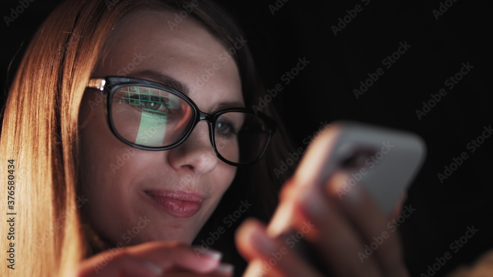 Beautiful young Woman Lying in Bed, Using Smart Phone and Smiling before Sleep. Woman using Cellphone on bed at Night. Attractive Girl looking at Mobile Phone. Beautiful young Woman Lying in Bed, Using Smart Phone and Smiling before Sleep. Woman using Cellphone on bed at Night. Attractive Girl looking at Mobile Phone.