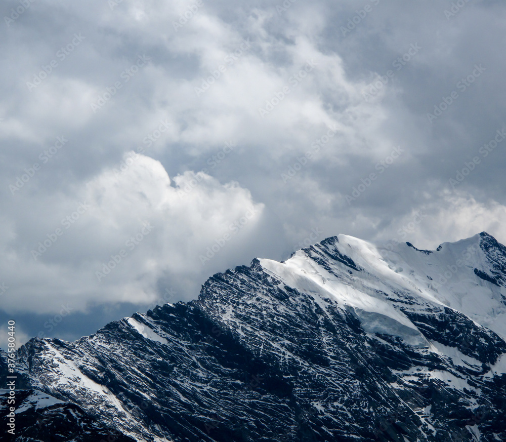 A close up of dramatic snow-capped Swiss Alp mountains in dappled light with moody clouds above in Switzerland