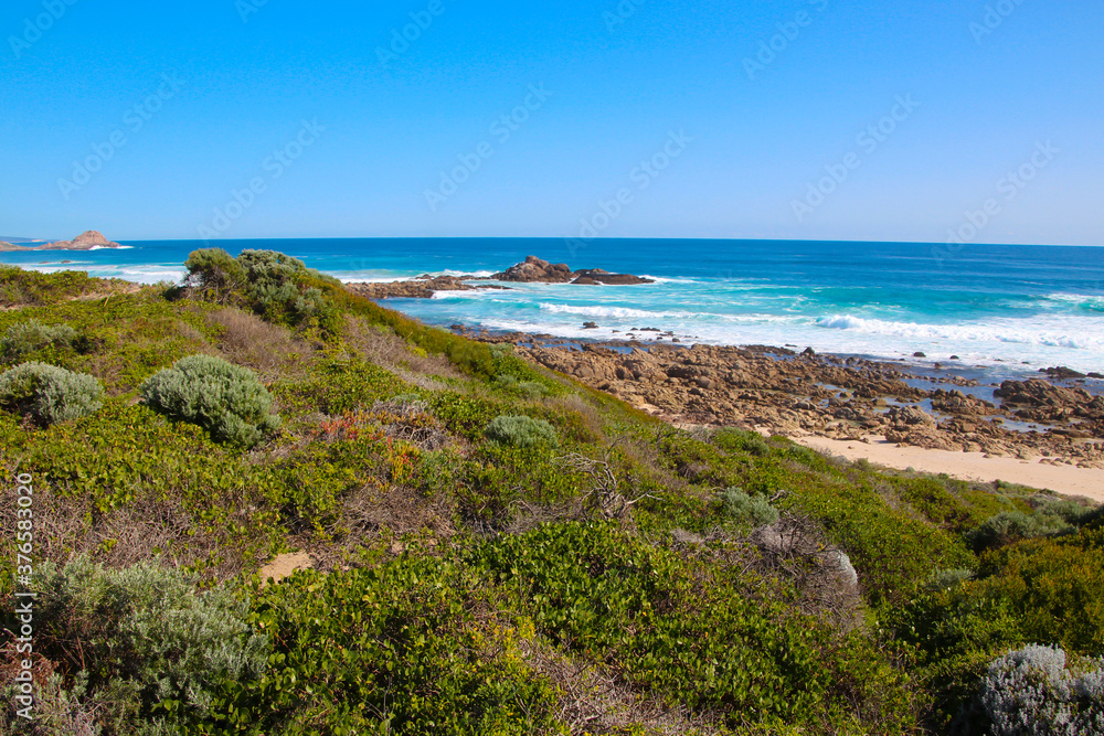 Scenic ancient Sugar Loaf Rock South Western Australia in the blue Indian Ocean is a popular fishing and hiking destination with its treeless green dunes and  splashing waves on old eroded rocks.