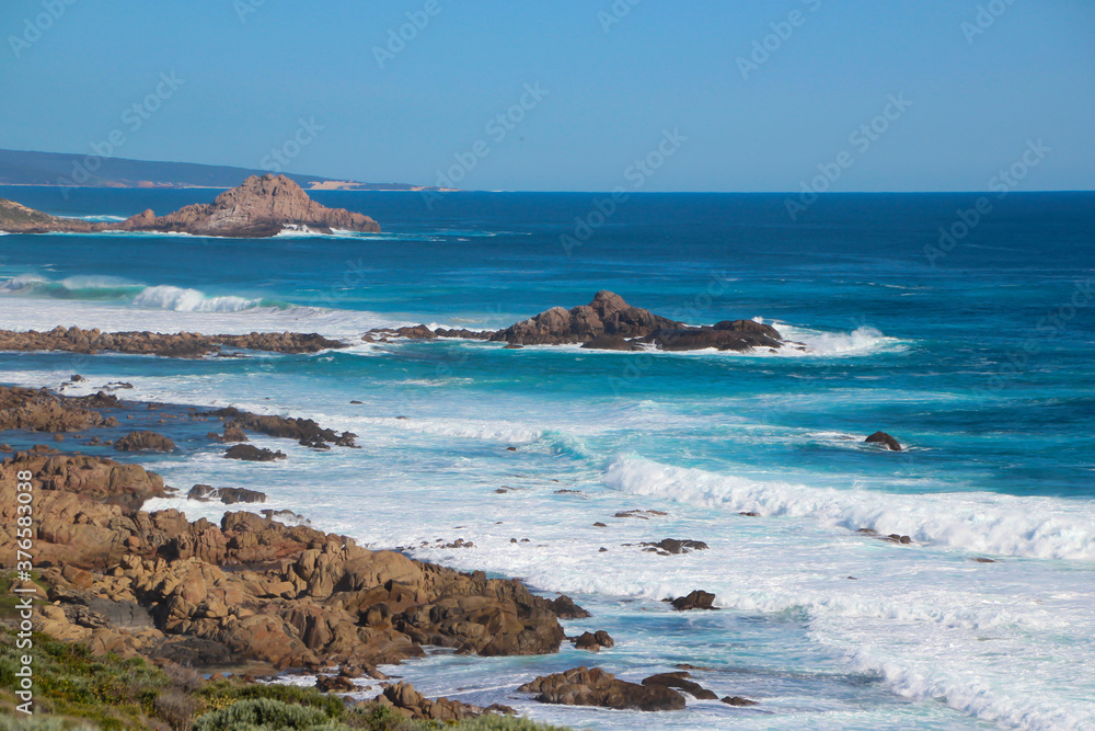 Scenic ancient Sugar Loaf Rock South Western Australia in the blue Indian Ocean is a popular fishing and hiking destination with its treeless green dunes and  splashing waves on old eroded rocks.