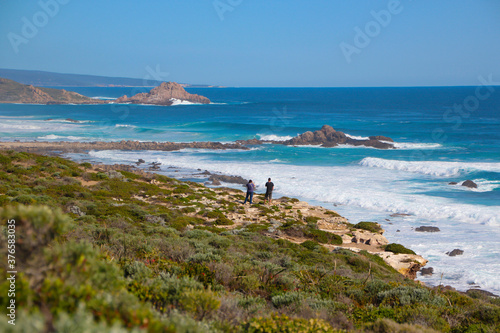 Scenic ancient Sugar Loaf Rock South Western Australia in the blue Indian Ocean is a popular fishing and hiking destination with its treeless green dunes and  splashing waves on old eroded rocks.