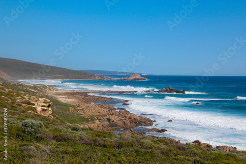 Scenic ancient Sugar Loaf Rock South Western Australia in the blue Indian Ocean is a popular fishing and hiking destination with its treeless green dunes and splashing waves on old eroded rocks.