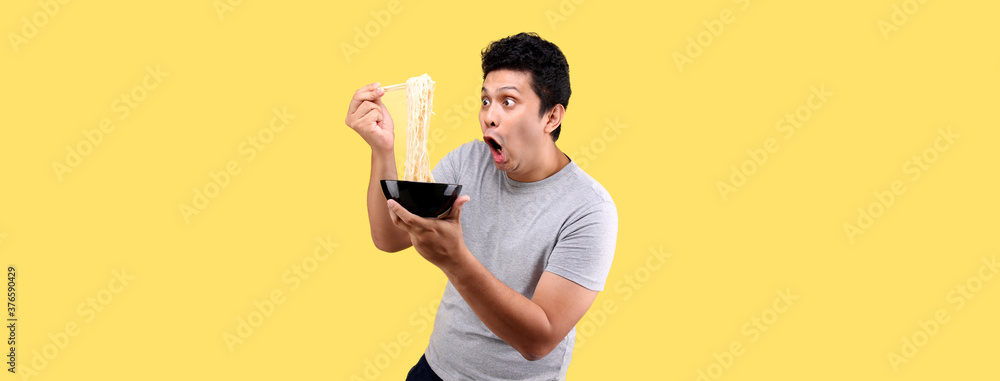 Close up Asian man eating yummy hot and spicy instant noodle using chopsticks and bowl isolated on yellow background in studio With copy space. Close up Asian man eating yummy hot and spicy instant noodle using chopsticks and bowl isolated on yellow background in studio With copy space.