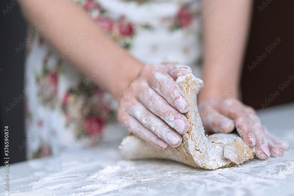 A young girl kneads dough with her hands on the table