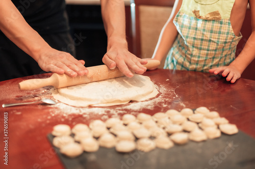 man rolls out the dough for dumplings. Child nearby helps. Close-up