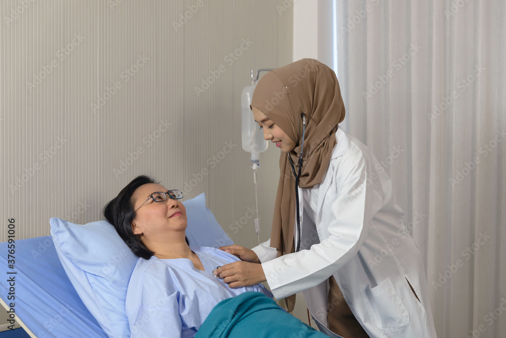 Young asian muslim female doctor using stethoscope checking to elderly patient sitting in bed at hospital. Medicine and health care safe concept Young asian muslim female doctor using stethoscope checking to elderly patient sitting in bed at hospital. Medicine and health care safe concept