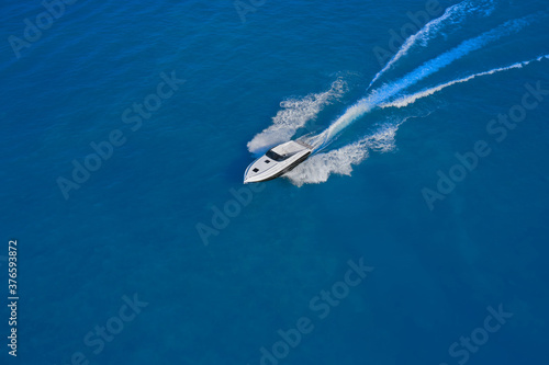 luxury motor boat. Top view of a white boat sailing in the blue sea. Drone view of a boat sailing at high speed. Aerial view of a boat in motion on blue water.