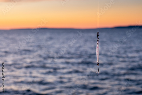 A fishing lure dangles from a fishing line with an sunset ocean backfdrop