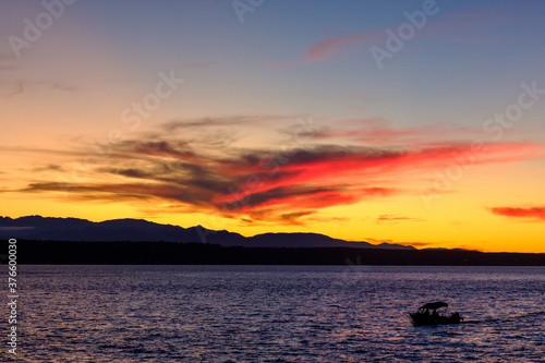 The clouds reflect the colorful sunset over Puget Sound as the sun slowly sets behind the mountains