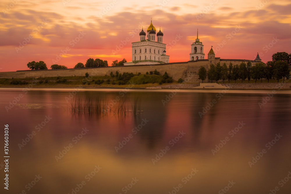 View of the Pskov Kremlin at sunset. Purple sky, blurred reflection in the river.