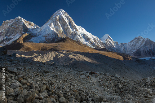 Pumori mountain in the Himalayas lit by the rising sun. Clear blue sky, a dark valley in the foreground. No people