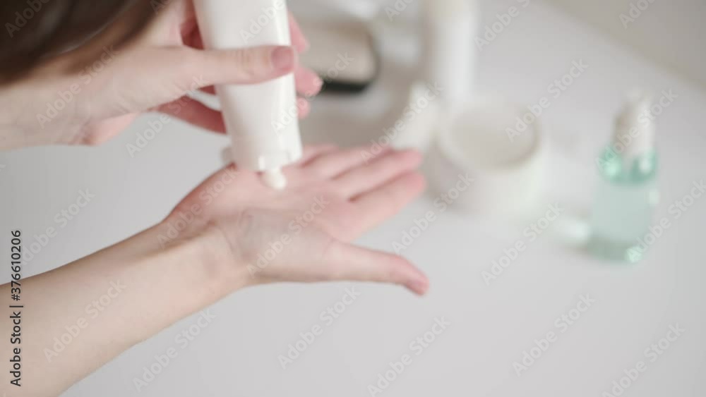 custom made wallpaper toronto digitalThe woman takes a plastic tube of cream from the white table and smears her hands. Hand skin care at home. Moisturizing lotion with vitamins, body care. Cosmetic beauty skincare product.