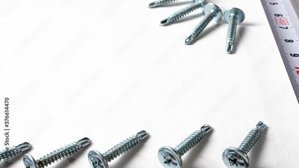 Self-tapping screw and measuring roulette on a white background banner with space for text. Construction tools, fastening hardware. Self-tapping screw and measuring roulette on a white background banner with space for text. Construction tools, fastening hardware.