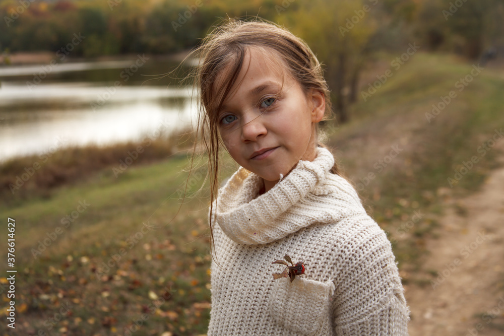 Portrait of preteen female kid resting in the park at warm autumn weather.  Girl wearing fall style clothes and playing with leaves.
