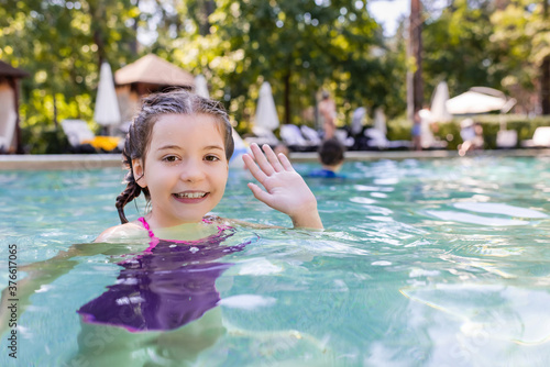 joyful girl in swimming pool looking at camera and waving hand © LIGHTFIELD STUDIOS