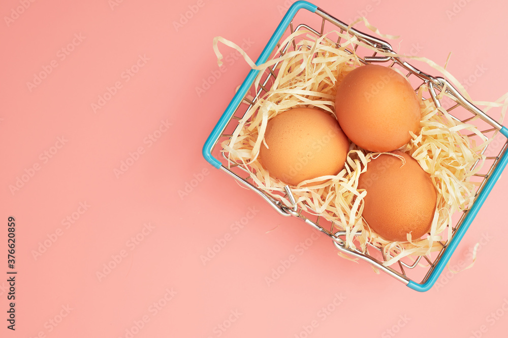 chicken eggs in a shopping cart on a pink pastel background, copy space, flatlay