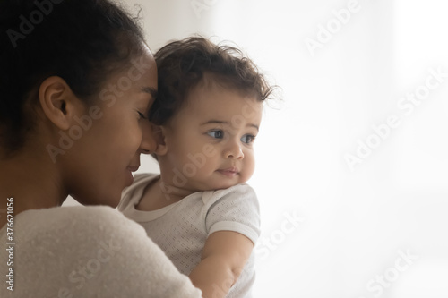 Close up head shot loving young african ethnicity woman holding embracing cute sweet infant child, enjoying sweet tender moment indoors, copy space for text, caring parents children concept.