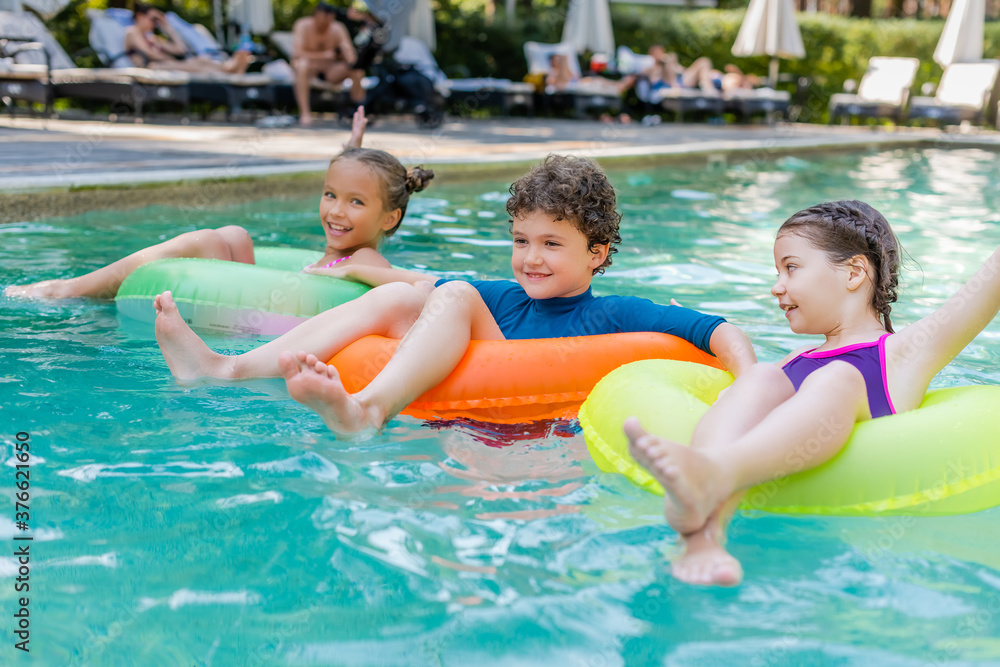 pleased boy and two girls swimming in pool on colorful inflatable rings