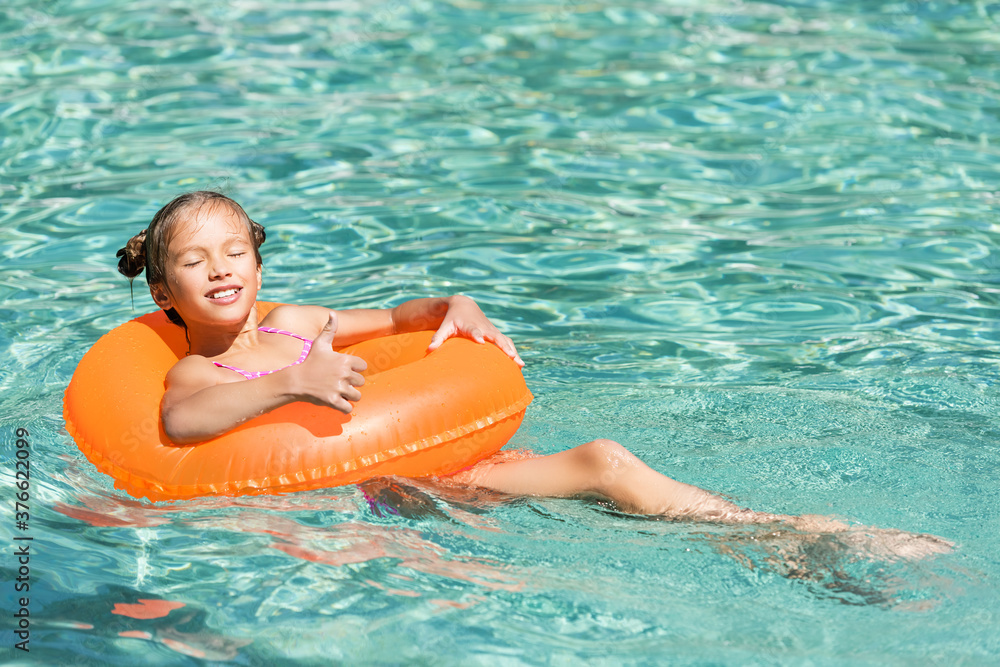 pleased girl showing thumb up while floating in pool on swin ring with closed eyes