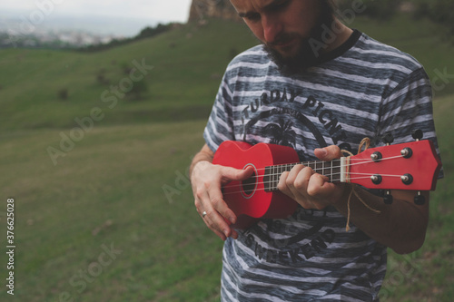 young man with red ukulele on green field of caucasus photo