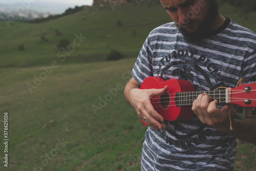 young man with red ukulele on green field of caucasus photo