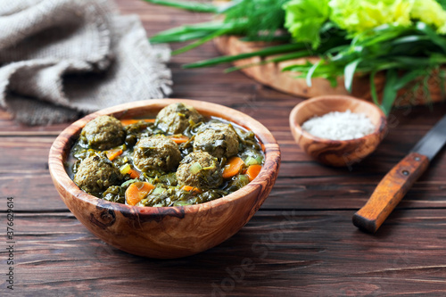 Soup with meatballs, vegetables and herbs in wooden bowl, selective focus photo