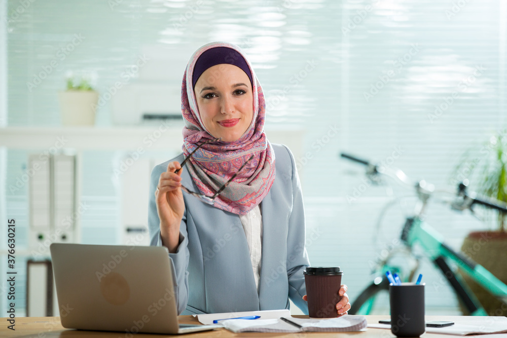 Beautiful young working woman in hijab and suit sitting in office ...