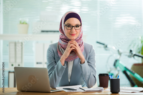 Fotografia Beautiful young working woman in hijab and suit sitting in office, smiling